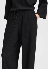 Pantaloni neri a coste con vita elastica e coulisse, gamba ampia e texture morbida. Realizzati in tessuto leggero.