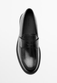 Black leather slip-on shoe with a rounded toe, stitched detailing, and a decorative band across the instep. Smooth texture and minimalist design.