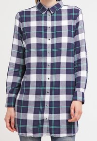 Navy and white checkered long-sleeve shirt with green accents, featuring a button-up front and a collar, made from soft fabric.