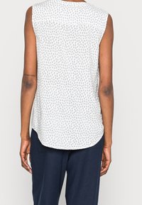 Top bianco senza maniche con una stampa animale grigia chiara, orlo arrotondato e una texture liscia. Abbinato a pantaloni scuri, che mostrano una vestibilità rilassata.