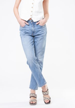 Jeans di denim azzurro chiaro con una vestibilità comoda e taglio dritto, abbinati a sandali con il tacco a forma di cuneo neri e bianchi a fantasia.