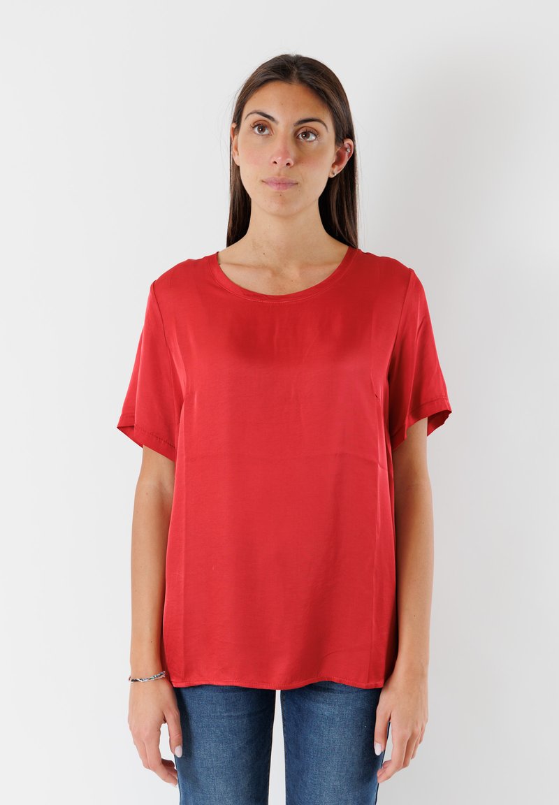 Top rosso a maniche corte in tessuto morbido con scollatura rotonda e vestibilità rilassata. Orlo dritto con una leggera caduta. Indossato con jeans blu.