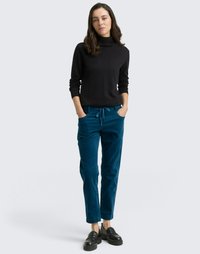 Black ribbed turtleneck sweater, paired with teal corduroy trousers with drawstring. Chunky black shoes complete the outfit.