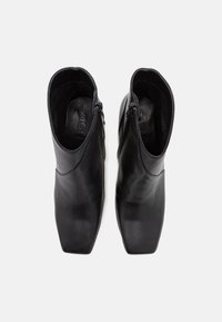 Bottines en cuir noir avec un bout carré, fermeture éclair de chaque côté et texture lisse. L'intérieur présente des détails de marque.