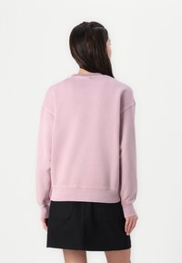 Ljusrosa sweatshirt med avslappnad passform, ribbade mudd och fåll. Utrustad med rundad halsringning och utan synliga tryck. Svart kjol under.