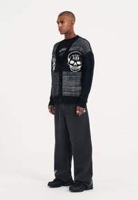 Černý a šedý pletený cardigan s designem lebek, zapínání na knoflíky a žebrovanými manžetami, spárovaný s volnými černými džíny a černými teniskami.