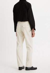 Krämfärgade byxor med rak passform, tillverkade av bomull. Matchas med en svart skjorta med en enkel design och svarta skor.