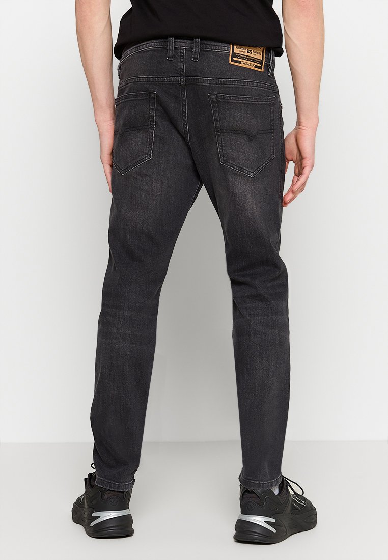 Schwarze Denim-Jeans mit Slim Fit, ausgestattet mit Gesäßtaschen und einem Lederschild am Bund. Strukturierter Stoff mit leichtem Farbverlauf.