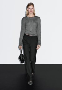Gray long-sleeve shirt with a relaxed fit, paired with high-waisted black trousers and gray pointed shoes. Holds a black handbag.
