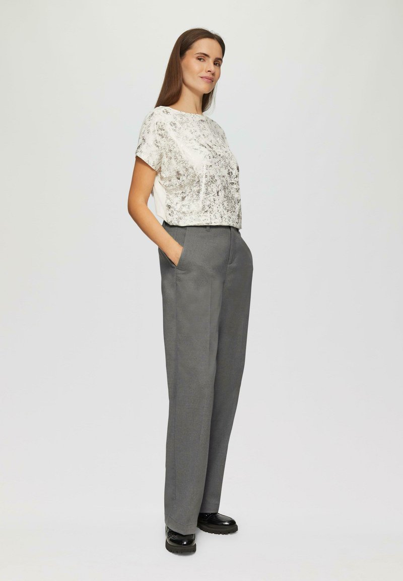 Haut à manches courtes à motif métallique associé à un pantalon gris taille haute. Le pantalon a des poches latérales ; porté avec des chaussures noires.