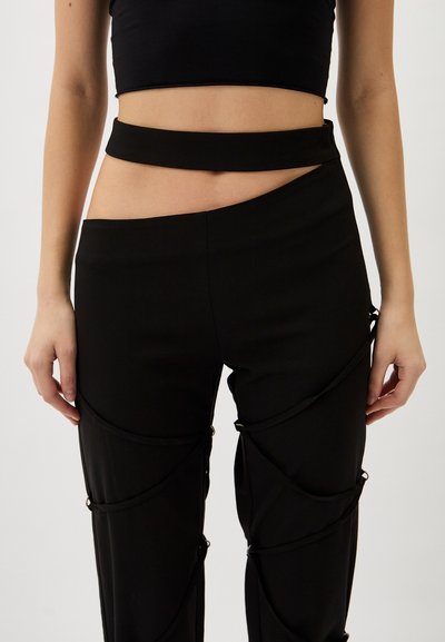 Black high-waisted pants with cutout details and thin ties, featuring smooth fabric and a fitted silhouette.