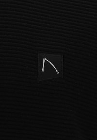 Schwarzer gerippter Stoff mit einem quadratischen Patch, der ein weißes geometrisches Design zeigt. Die strukturierte Oberfläche hat eine subtile Tiefe. Schlicht, monochromatisch im Stil.