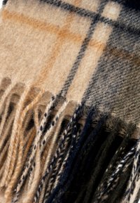 Écharpe en plaid en laine beige et marine, présentant un motif à carreaux avec des touches d'orange, finie par des bords frangés pour ajouter de la texture.