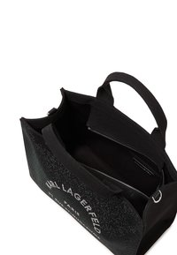Sac fourre-tout noir avec une texture tissée, arborant un logo argenté. Il est doté de doubles poignées et d'une poche intérieure zippée pour un rangement sécurisé.