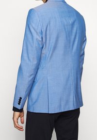 Blazer azzurro chiaro realizzato in tessuto testurizzato. Presenta una vestibilità su misura, revers a contrasto e quattro accentuazioni con bottoni neri sulle maniche.