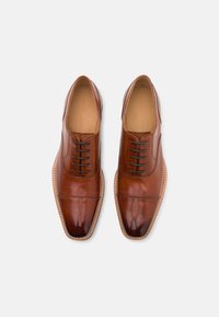 Zapatos de vestir de cuero marrón con un acabado pulido, puntera redondeada, seis ojales y con un pespunteado en el filo. Textura suave y diseño elegante.