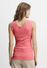 Top in cotone coral ribbed con pizzo lungo il collo a giro e le aperture delle maniche, caratterizzato da una silhouette aderente e un orlo scallop.