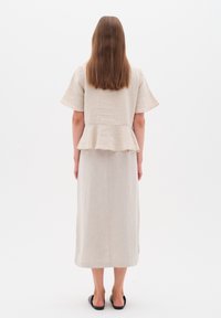 Beige lněné šaty s peplum lemem, krátkými rukávy a rovnou siluetou, nošené s černými sandály. Minimalistický design a viditelná textura.