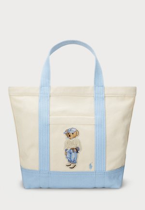 Sac fourre-tout en toile beige avec des poignées bleu clair, décoré d'un ours brodé portant un pull et une casquette, avec un panneau inférieur bleu.