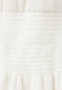 Gros plan d’un tissu blanc avec une texture smockée élastique froncée et un bord volanté en bas.