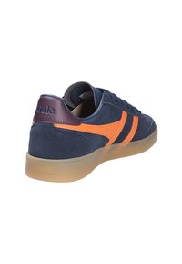 Mörkblå mocka sneakers med orange läderdetaljer och två ränder. Har en mörkbrown hälflik med präglad logotyp och sula av gummi.