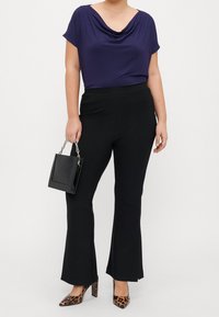 Mörkblå polokrage-topp, svarta utsvängda byxor och klackar med leopardmönster. Outfiten kompletteras av en liten svart handväska med kedjerep.