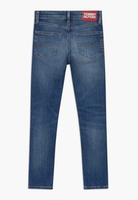 Modré džíny z denimu s přiléhavým střihem, pěti kapsami a viditelnou logo nášivkou na zadním pásu. Hladká textura s mírným ztracením barvy.