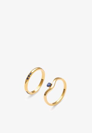 Zwei goldene Ringe, einer mit drei kleinen blauen Steinen entlang des Rings, der andere mit einem einzelnen runden blauen Stein auf einem gebogenen Ring.