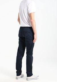 Tmavě modré kalhoty z odolné látky, s úzkým střihem, detailem zadní kapsy a doplněné bílými teniskami a jednoduchým bílým tričkem.