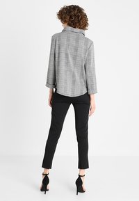 Gray plaid jacket with a collar, three-quarter sleeves, and a rounded hem, paired with black slim-fit trousers and black high-heeled shoes.