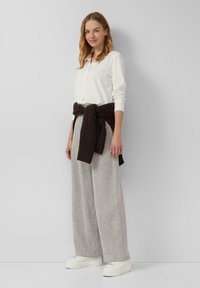 Weißes Hemd mit Knöpfen, breite graue strukturierte Hose, dunkelbrauner Pullover um die Taille gebunden, weiße Sneaker. Schlichtes und lässiges Design.