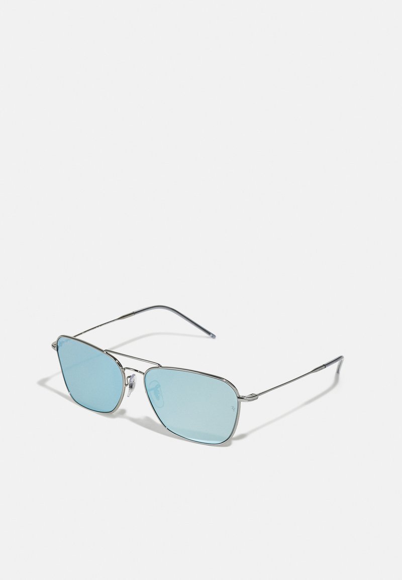 Ochelari de soare din metal argintiu cu lentile albastre, formă rectangulară, brațe subțiri și pernuțe pentru nas ajustabile. Design minimalist fără logo-uri vizibile.