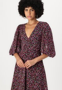 Robe florale avec un décolleté en V profond et des manches bouffantes. Fond noir avec de petites fleurs roses, orange et blanches. Tissu doux et léger.