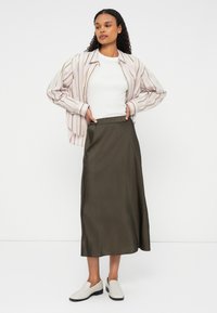 Garšīga oliņu zaļas satīna svārki ar elastīgu jostu, apvienoti ar baltu augšu un daudzkrāsainu svītrainu krekliņu ar pogām. Baltas slaidas apavus.