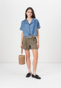 Kortärmad cropped denimskjorta, knuten i midjan; kombinerad med olivgröna shorts och en vävd korgväska. Svarta skor.