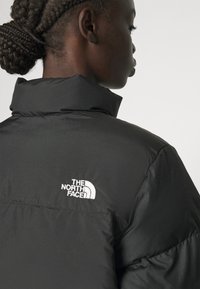 Giacca nera isolata con colletto alto, texture trapuntata e il logo bianco di 'The North Face' sulla schiena.