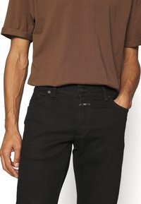 Černé džíny slim fit vyrobené z denimu. V kombinaci s hnědým tričkem s krátkým rukávem. Obsahuje zapínání na knoflík a přední kapsy.