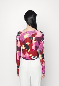Ribbed svetr v živém květinovém vzoru s převládajícími červenými, růžovými a žlutými barvami. Má dlouhé rukávy a čtvercový výstřih.