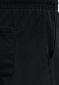 Zwarte sportieve broek heeft een zachte, gestructureerde stof met een elastische tailleband en een zijzak aan de linkerzijde, waardoor een strakke uitstraling ontstaat.
