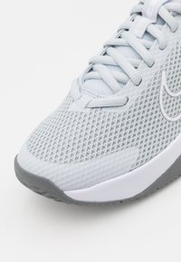 Scarpa da ginnastica grigia chiara con tomaia in rete, superficie testurizzata e suola in gomma con un logo bianco sottile. Design con lacci per una vestibilità sicura.