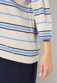 Raidallinen yläosa vaaleanbeigellä pohjalla, jossa on tummansinisiä ja taivaansinisiä vaakasuoria raitoja, rento istuvuus ja kolmanneksen pituiset hihat.