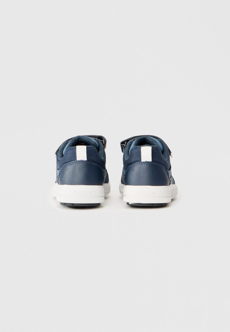 Baskets bleu marine en matériaux textile et cuir, avec une semelle blanche, une sangle en velcro et un petit accent blanc à l'arrière. Vue arrière présentée.