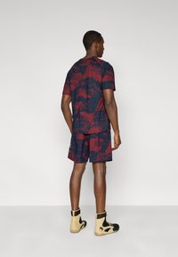 Αθλητική στολή που περιλαμβάνει ένα μπλε σκούρο ναυτικό και βουργουνδί κοντομάνικο πουκάμισο με σχέδια και αντίστοιχα σορτς, σε συνδυασμό με μπεζ και μαύρα παπούτσια υψηλού λαιμού.