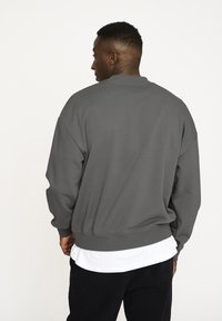 Gray sweatshirt with a ribbed crew neckline, wide sleeves, and a relaxed fit, worn over a white shirt. Texture appears soft and smooth.