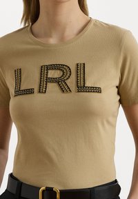 Beige kortermet t-skjorte med rund hals krage, med svart brodert "LRL" tekst og med geometriske mønstre.