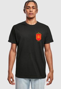 Sort bomulds-t-shirt med et rødt og gult Spanien-emblem med en krone og året "2024" på venstre bryst. Korte ærmer, rund hals.