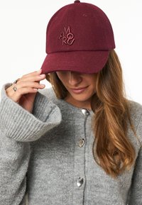 Chapeau bordeaux en feutre, avec un design brodé. Le chapeau a une visière courbée et des œillets pour la ventilation.