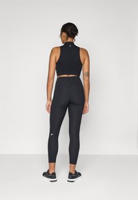 Top corto sportivo nero e leggings a vita alta, entrambi realizzati in tessuto traspirante; design aderente con logo discreto sulla gamba.