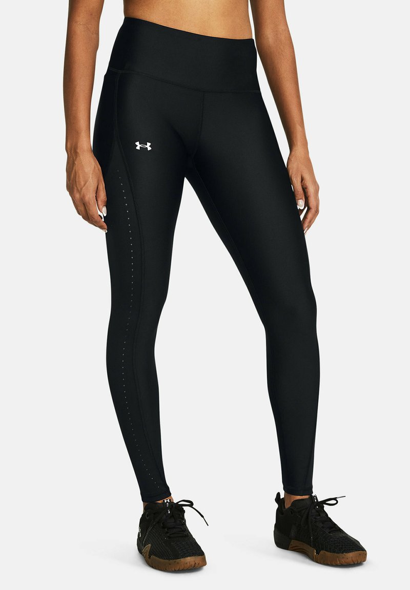 Leggings deportivos negros con una cintura alta, textura suave y una costura lateral con pequeños acentos de puntos. Combinados con zapatillas deportivas negras.
