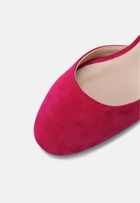 Chaussure en daim rose vif avec bout arrondi et motif ajouré sur le côté. Doublure intérieure lisse, mettant en valeur une texture douce.